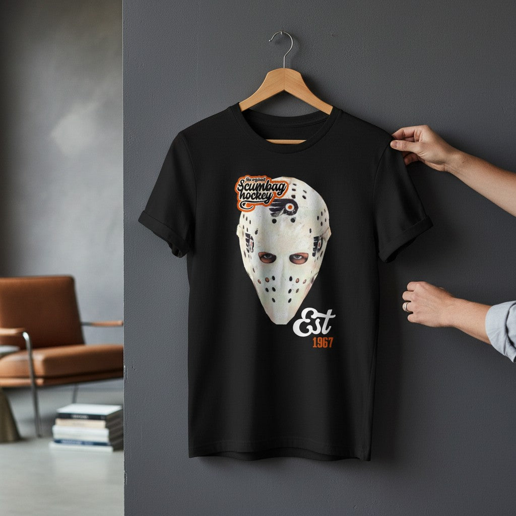 Black t-shirt with hockey mask graphic and text on a hanger against a gray wall.