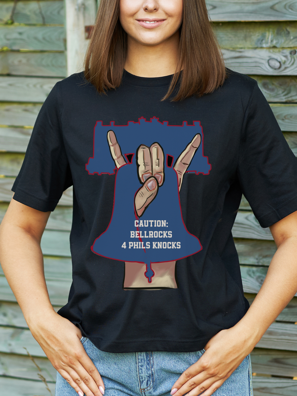 womans in black t-shirt with a bold graphic of a hand gesture forming a bell shape inside a Liberty Bell outline, with text that reads “Caution: Bellrocks 4 Phils Knocks